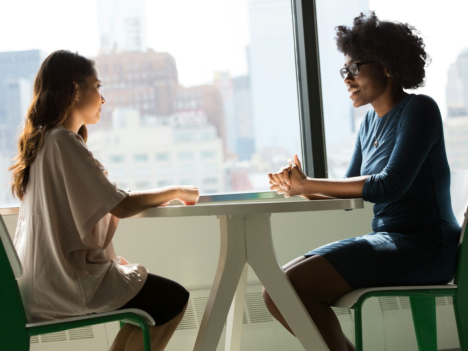 Twee vrouwen in gesprek aan een tafel bij het raam
